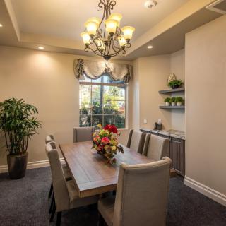 A cozy and elegant dining room featuring a large wooden table, comfortable upholstered chairs, a decorative chandelier, and lush green plants.