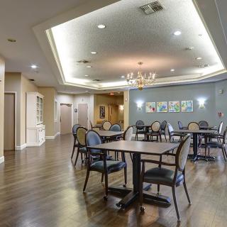 A spacious dining area with elegant tables and chairs, featuring polished wood flooring and ambient ceiling lighting.