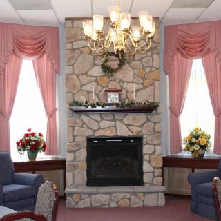 A cozy living room with a stone fireplace, elegant chandelier, and pink curtains.