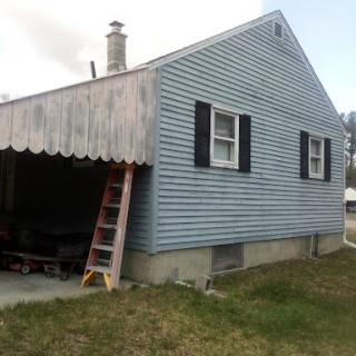 A side view of a blue house with a ladder leaning against it, showcasing the exterior and garage area.