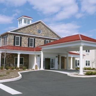 A building with a stone facade and red roof, featuring a covered entrance supported by columns.