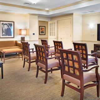A waiting room with rows of chairs facing a television, decorated with framed artwork.