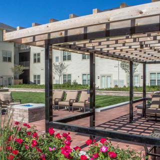 A pergola with outdoor seating surrounded by a garden in an apartment complex.