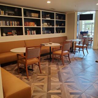 A cozy and modern cafe seating area with tables, chairs, and a bookshelf lining the wall.