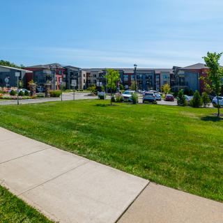 A well-maintained apartment complex with a green lawn and parked cars on a sunny day.