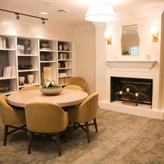 A cozy living room with a round dining table, chairs, a fireplace, and bookshelves.