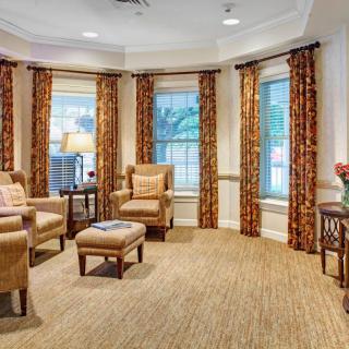 A cozy living room with comfortable chairs, patterned curtains, and large windows.