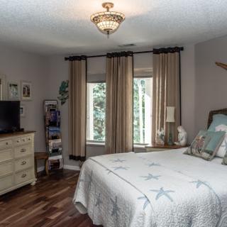 A cozy bedroom featuring a comfortable bed, stylish curtains, and warm wooden flooring.