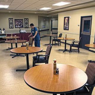 A custodian is cleaning an empty dining area with multiple tables and chairs.