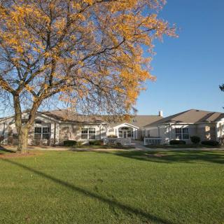 A sunny view of a residential house with an autumn tree and green lawn.