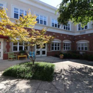 A school courtyard with benches, trees, and a brick-faced building.