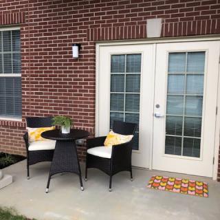 A cozy patio setup with wicker chairs and a small table against a brick wall near French doors.