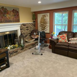 A cozy living room featuring a fireplace, comfortable sofa, and an exercise bike by the window.