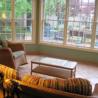 A cozy living room with large windows, allowing natural light and a view of the greenery outside.