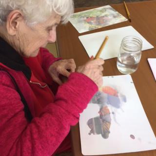 An elderly person engaged in watercolor painting at a table.