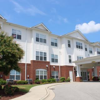 A residential building with brick and white siding, featuring a covered entrance and neatly landscaped surroundings.