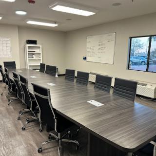 A spacious conference room equipped with a long meeting table and several ergonomic chairs, featuring a whiteboard and natural light from a window.