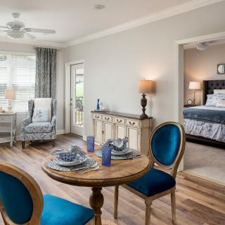 A cozy living space featuring a dining table with blue chairs, elegant decor, and an adjoining bedroom.