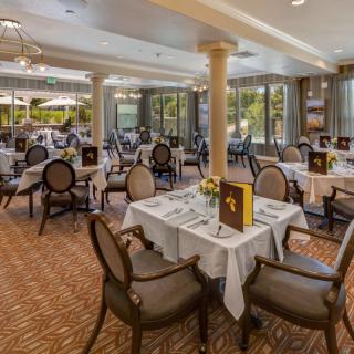 An elegant dining room with neatly arranged tables and chairs, featuring large windows that offer a pleasant view.
