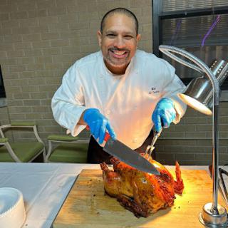 A chef joyfully carving roasted meat in a professional kitchen setting.