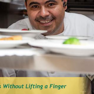 A smiling chef looks through a serving counter in a restaurant kitchen.