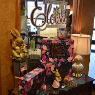 A charming display featuring Eloise-themed decor and colorful gift boxes, complemented by decorative figurines and a warm lamp.