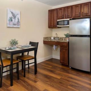 A compact kitchen space with a dining table and chairs, featuring wooden cabinets, a stainless steel refrigerator, and a microwave.