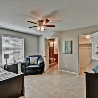 A spacious bedroom with a comfortable chair, ceiling fan, and ample natural light. The room features a walk-in closet visible in the background.