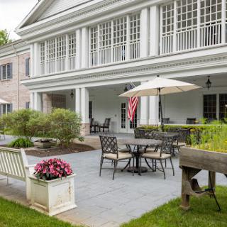 A serene outdoor patio space featuring comfortable furniture, a decorative umbrella, and vibrant flowers, surrounded by a well-maintained lawn.