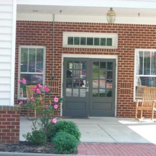 The image shows the entrance to a brick building with glass doors, windows, and flowers.