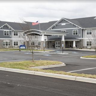 A large building with a parking area and an American flag in front, set against an overcast sky.