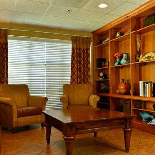 A cozy living room with armchairs, a wooden coffee table, and a bookshelf beside a large window.