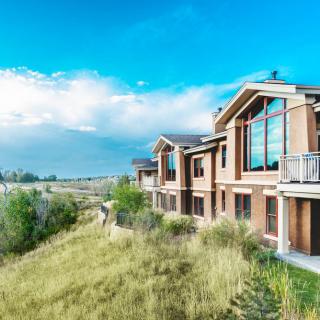 A modern house with large windows overlooking a grassy landscape under a blue sky.