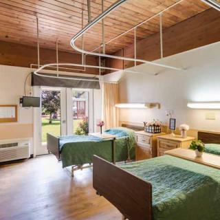 A well-lit hospital room with two patient beds, featuring a serene view of the garden outside.
