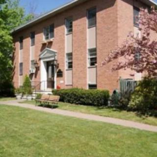 A brick residential building with a neatly trimmed lawn and trees, showcasing a spring setting.
