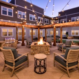 A cozy outdoor patio with a firepit, surrounded by comfortable seating and illuminated by string lights.