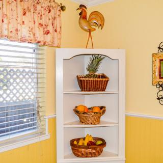 A cozy kitchen corner featuring a white shelf adorned with fruit baskets and a rooster decoration.