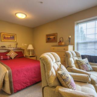 Cozy bedroom with a red bed, two armchairs, and warm lighting.