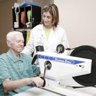 An elderly man engages in a physical therapy session with a healthcare professional assisting him.