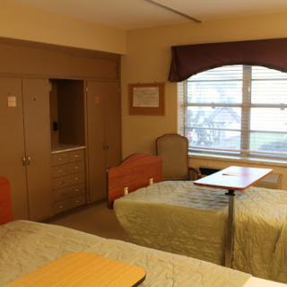A simple and functional room featuring two beds, a window with natural light, and minimalistic decor.
