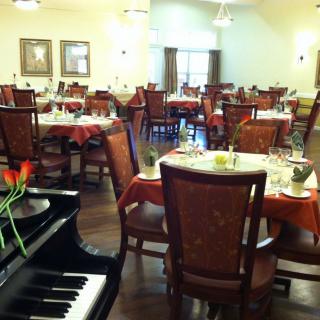 A warmly lit dining area with elegantly set tables and a piano in the foreground.
