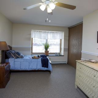 A cozy bedroom with a single bed, dresser, and a large window letting in natural light.