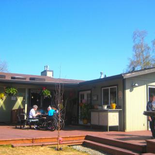 A sunny day at an outdoor cafe with people sitting on a wooden deck.