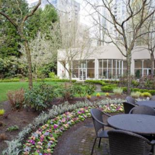 A serene garden with outdoor seating surrounded by lush greenery and colorful flowers in an urban setting.