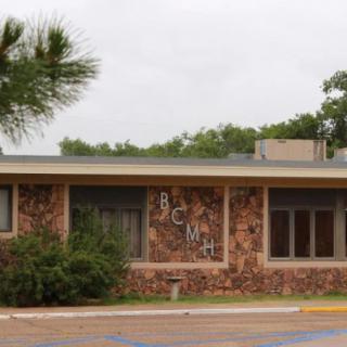 A single-story building with a brick facade and large windows, featuring graffiti on the wall, surrounded by trees.