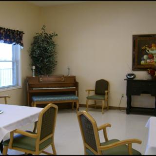 A cozy room with a piano, chairs, and tables, featuring a window and decorative elements.