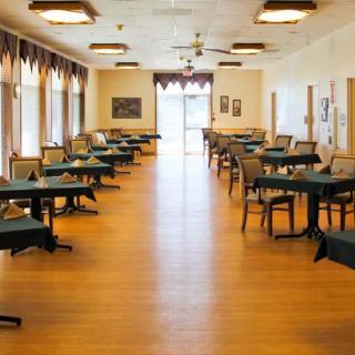 An empty dining room with neatly arranged tables and chairs, featuring large windows and a wooden floor.