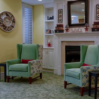 A cozy living room with two green armchairs, a fireplace, and decorative shelves.