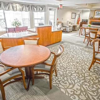 A spacious and bright dining area with wooden tables and chairs, featuring large windows and patterned carpet.