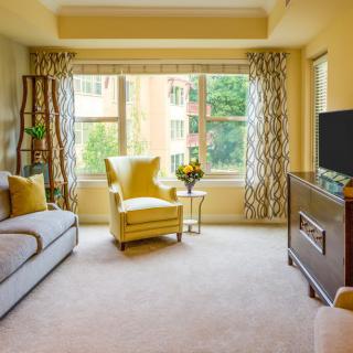 A cozy living room with a modern design, featuring a yellow armchair, sofa, and large window with patterned curtains.
